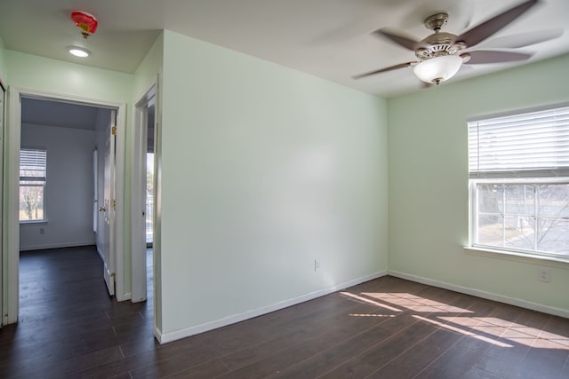 spare room with a wealth of natural light, baseboards, dark wood finished floors, and a ceiling fan