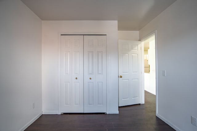 unfurnished bedroom with dark wood-style floors, a closet, and baseboards