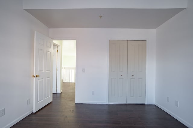 unfurnished bedroom with a closet, baseboards, and dark wood-style flooring