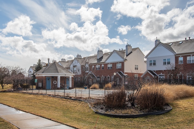 exterior space featuring a front lawn, fence, brick siding, and a residential view