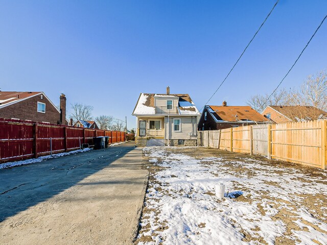 snow covered house featuring a fenced backyard