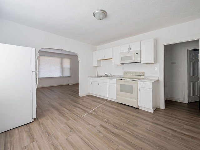 kitchen featuring white appliances, baseboards, arched walkways, white cabinetry, and light wood-type flooring