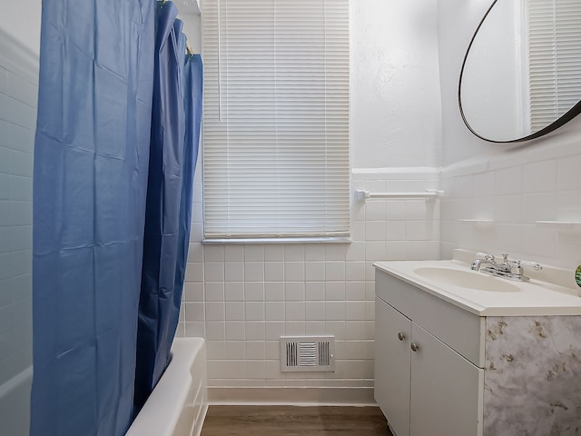 full bath featuring visible vents, shower / bath combo with shower curtain, wood finished floors, tile walls, and vanity