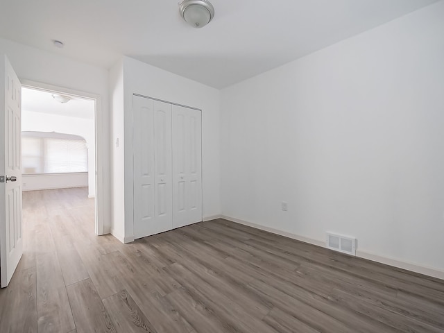 unfurnished bedroom with a closet, visible vents, baseboards, and wood finished floors