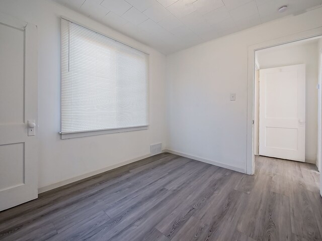 empty room featuring a healthy amount of sunlight, wood finished floors, visible vents, and baseboards