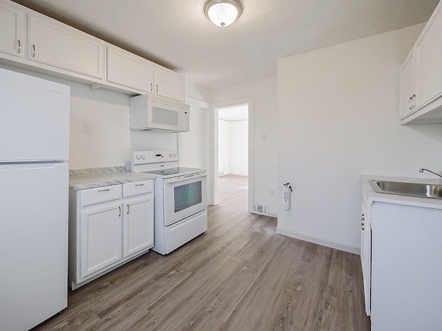 kitchen with light countertops, light wood-style flooring, white cabinets, white appliances, and a sink