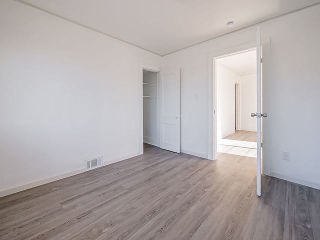 unfurnished bedroom with a closet, visible vents, baseboards, and wood finished floors