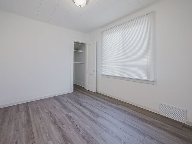 unfurnished bedroom with wood finished floors, visible vents, a closet, and baseboards