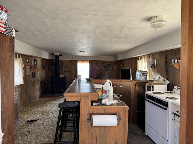 kitchen featuring a breakfast bar, white electric range, wood walls, dark colored carpet, and a wood stove