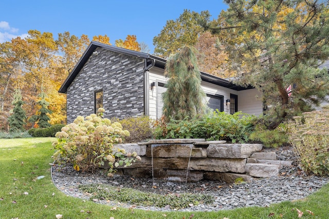 view of property exterior featuring a garage, stone siding, and a lawn