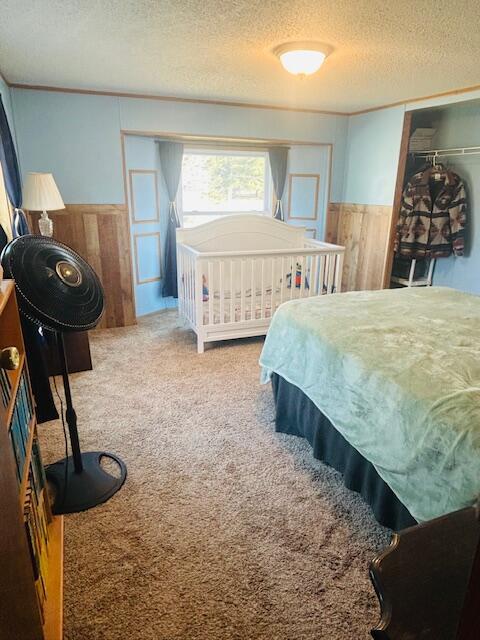 bedroom with a textured ceiling, carpet flooring, wood walls, and wainscoting