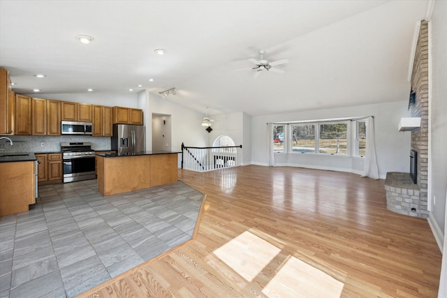 kitchen featuring lofted ceiling, a sink, appliances with stainless steel finishes, a brick fireplace, and open floor plan