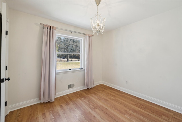 spare room featuring visible vents, baseboards, an inviting chandelier, and light wood-style flooring