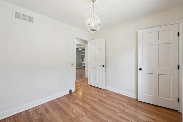 unfurnished bedroom featuring a chandelier, visible vents, light wood-style flooring, and baseboards