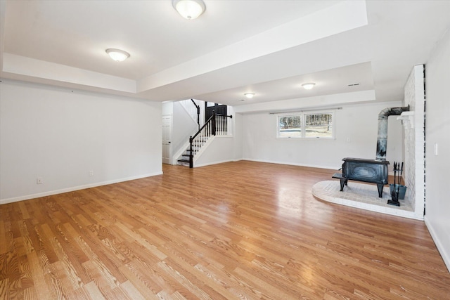 basement with stairs, a wood stove, light wood-style floors, and baseboards