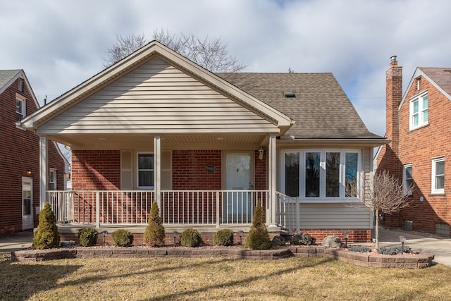 view of front of property with a front lawn, covered porch, roof with shingles, and brick siding