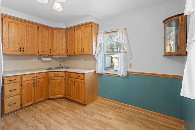 kitchen featuring light wood-type flooring, a sink, brown cabinetry, light countertops, and baseboards