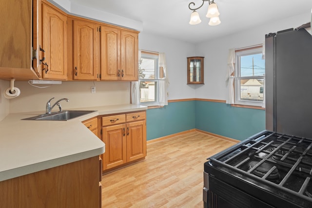 kitchen featuring light wood-type flooring, black gas range, a sink, an inviting chandelier, and light countertops