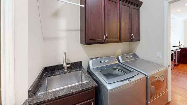 washroom featuring washer and dryer, cabinet space, light wood finished floors, and a sink