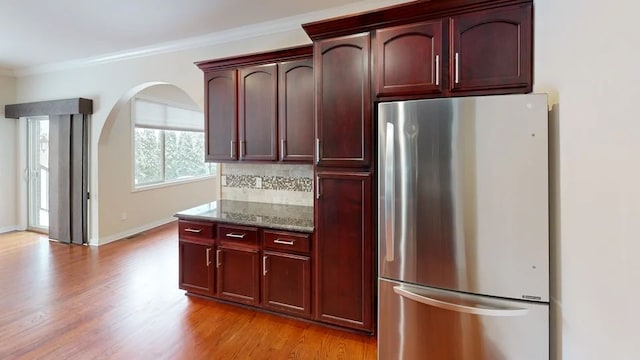 kitchen with light wood finished floors, dark brown cabinets, ornamental molding, dark stone countertops, and freestanding refrigerator