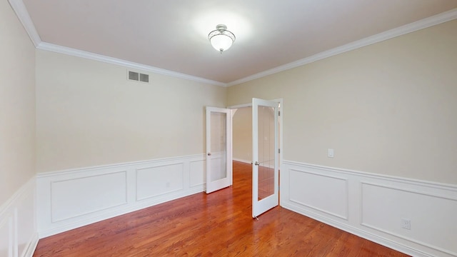 empty room featuring wood finished floors, visible vents, ornamental molding, french doors, and wainscoting