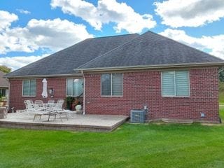 rear view of house with a patio, central AC unit, a lawn, and brick siding