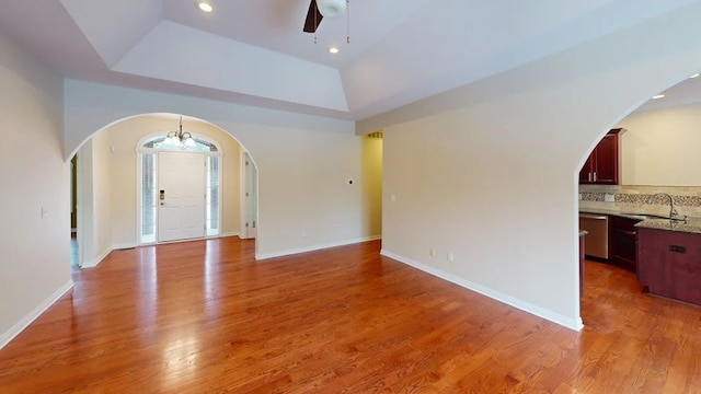 interior space featuring arched walkways, light wood-type flooring, baseboards, and a sink