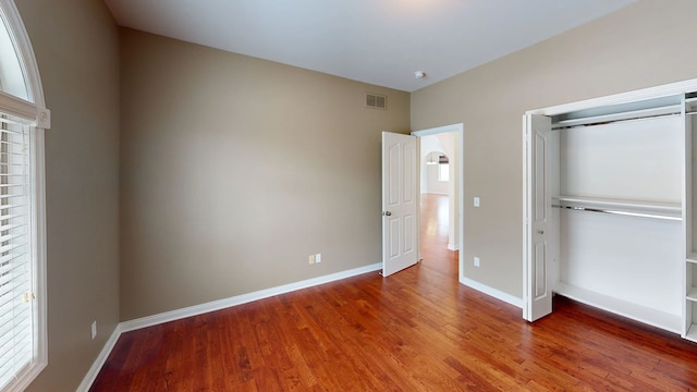 unfurnished bedroom featuring visible vents, baseboards, a closet, and wood finished floors