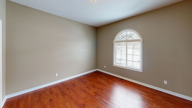 unfurnished room featuring visible vents, dark wood-style floors, and baseboards