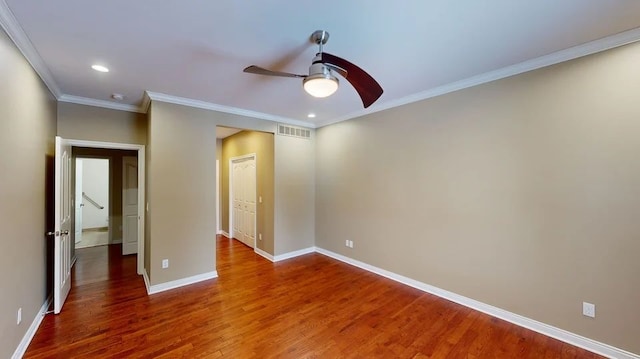 spare room with crown molding, wood finished floors, visible vents, and baseboards