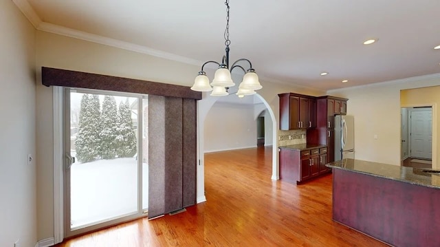 kitchen featuring light wood finished floors, tasteful backsplash, crown molding, freestanding refrigerator, and arched walkways