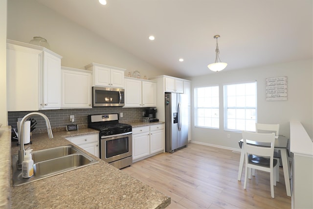 kitchen with vaulted ceiling, decorative backsplash, white cabinets, stainless steel appliances, and a sink