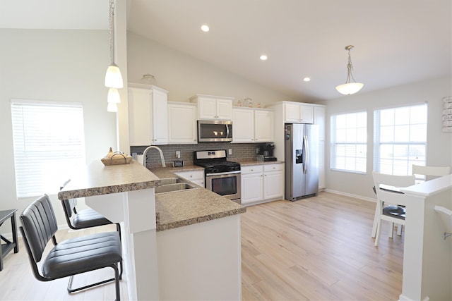 kitchen featuring light wood finished floors, a sink, hanging light fixtures, stainless steel appliances, and tasteful backsplash