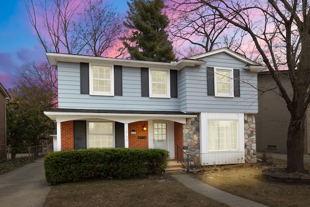 traditional-style house featuring stone siding, brick siding, a porch, and fence