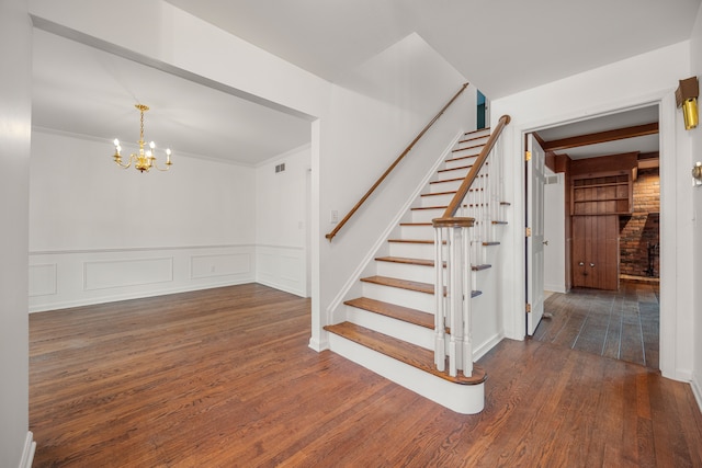 staircase featuring visible vents, ornamental molding, wood finished floors, wainscoting, and a chandelier