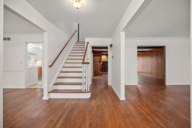 staircase with ornamental molding, wood finished floors, visible vents, and baseboards