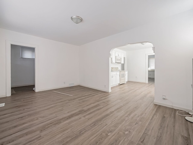 empty room featuring baseboards, arched walkways, and light wood-style flooring