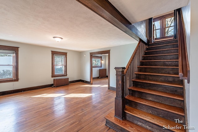 stairway with a wealth of natural light, baseboards, wood finished floors, and radiator heating unit