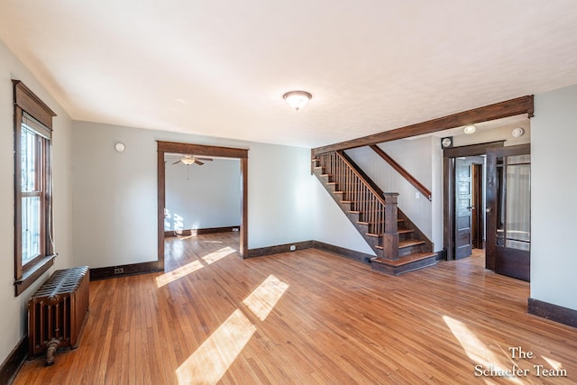 unfurnished living room featuring stairway, radiator, baseboards, and hardwood / wood-style flooring