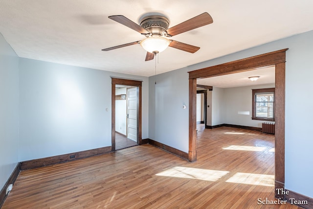 empty room with ceiling fan, radiator, light wood-type flooring, and baseboards