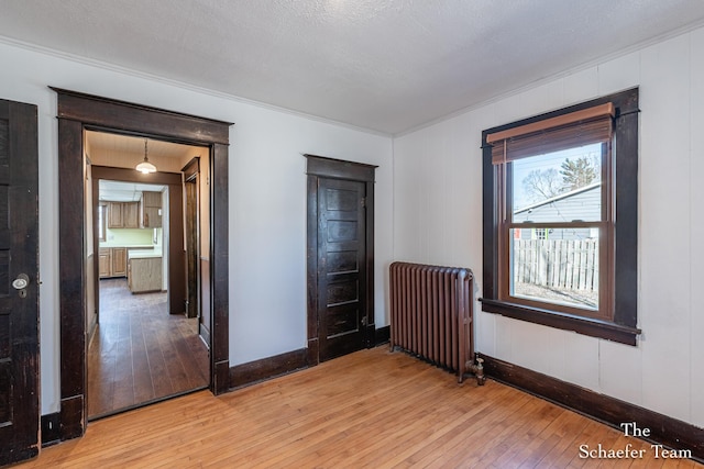 unfurnished bedroom with baseboards, radiator, crown molding, and light wood finished floors