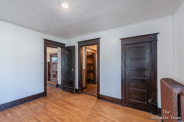 unfurnished room with light wood-style floors, radiator, stairs, and a textured ceiling