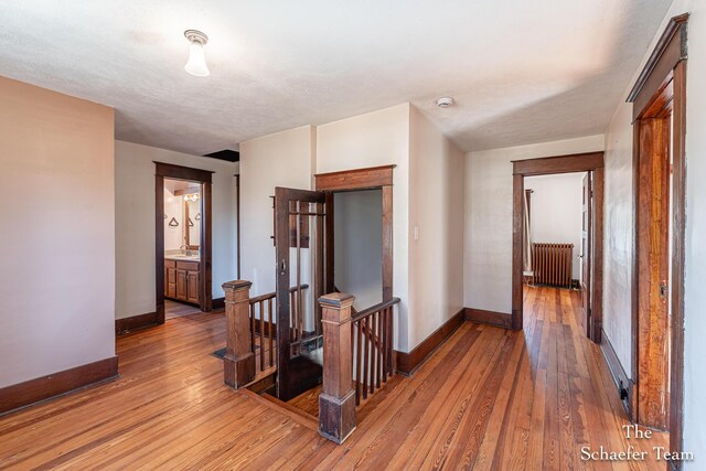 hallway with an upstairs landing, baseboards, radiator heating unit, and light wood-style floors