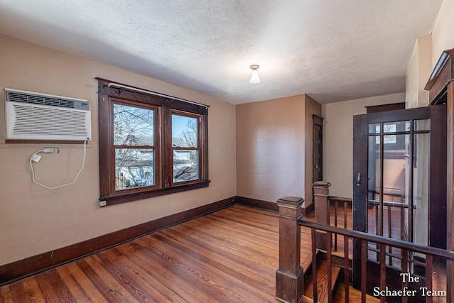 empty room featuring wood finished floors, baseboards, a wall mounted air conditioner, and a textured ceiling