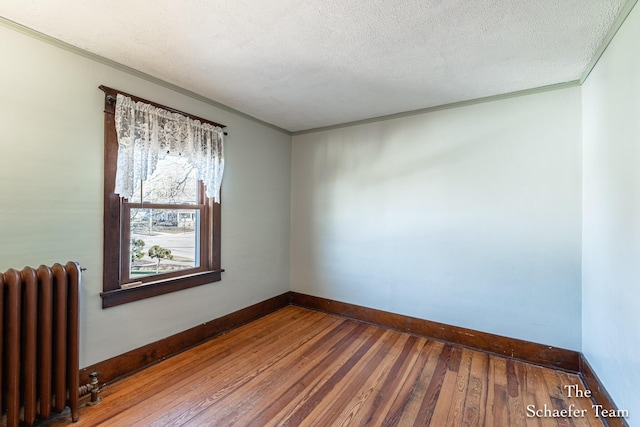 unfurnished room with baseboards, wood-type flooring, a textured ceiling, and radiator heating unit