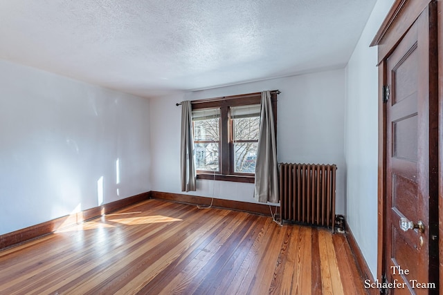 spare room featuring baseboards, a textured ceiling, radiator heating unit, and hardwood / wood-style flooring