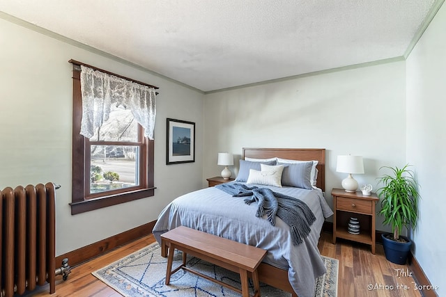 bedroom featuring radiator heating unit, wood finished floors, baseboards, and a textured ceiling