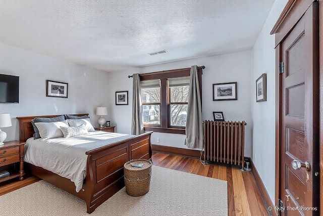 bedroom with visible vents, radiator, a textured ceiling, and wood finished floors