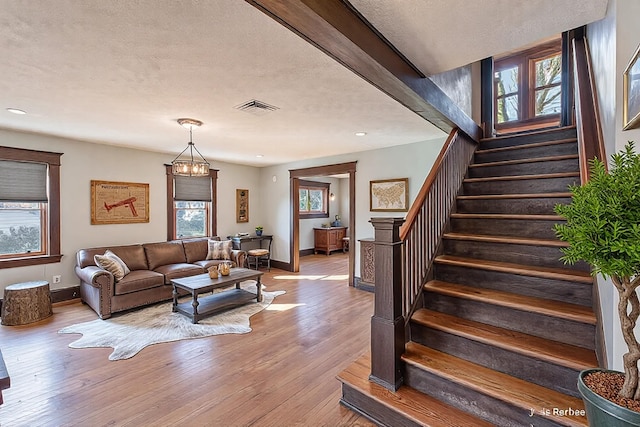 living area featuring wood finished floors, visible vents, baseboards, stairs, and a notable chandelier