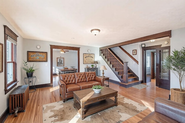 living area featuring baseboards, radiator, light wood-style flooring, and stairs